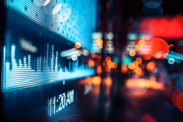 A digital display shows a blue stock market graph with blurred city lights in the background.